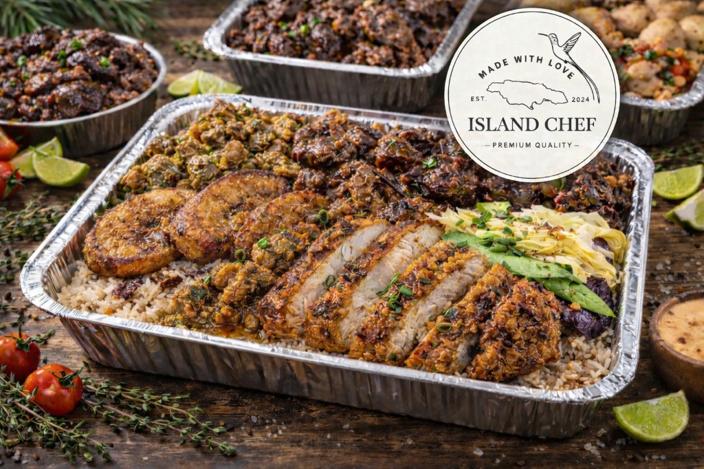 Island Chef Caribbean catering spread: rice and peas, golden sliced meat, fried plantain, stew and fresh vegetables on a wooden surface